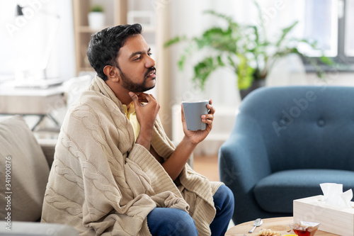 people, healthcare and problem concept - sick man with cup of tea touching his sore throat at home