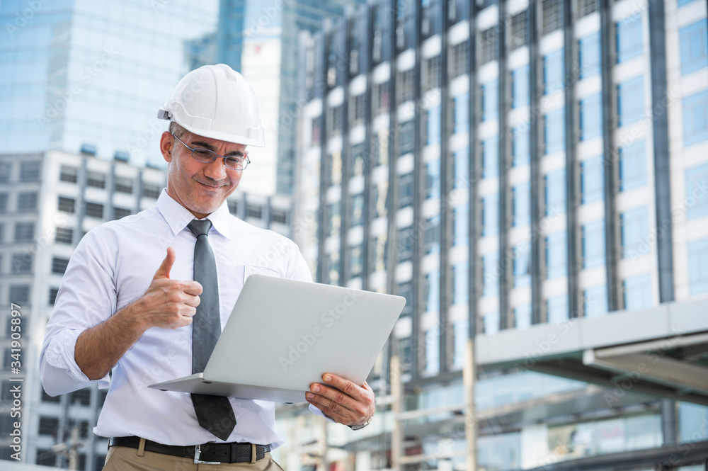 Civil engineering using laptop while working on building construction site and feeling happy with his project. Civil engineering using laptop while working on building construction site and feeling happy with his project.