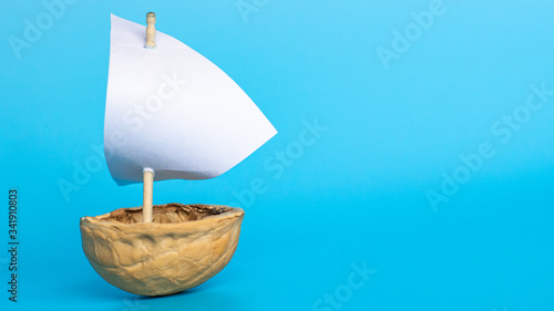a small boat made of nutshell with a white sail on the blue background. Journey banner template.