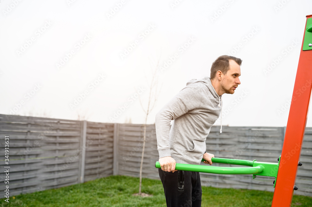 Athletic young man is doing exercises on parallel bars outdoors. Healthy lifestyle concept