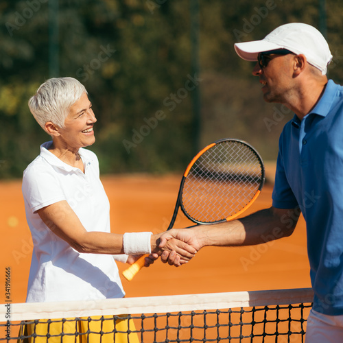 Tennis Instructor with Senior Woman in her 60s Handshaking after Having a Tennis Lesson on Clay Court.