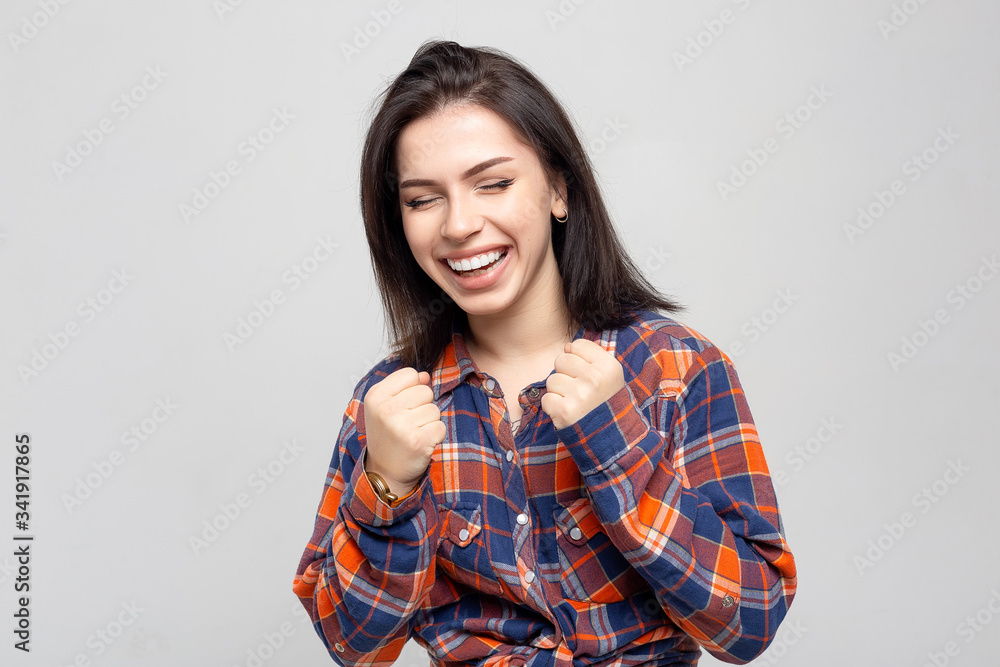 Beautiful young woman portrait. Portrait of a beautiful smiling brunette in a plaid shirt on a white-gray Beautiful young woman portrait. Portrait of a beautiful smiling brunette in a plaid shirt on a white-gray