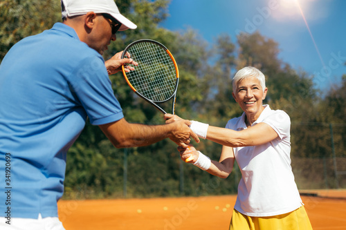 Senior Woman Training with Tennis Instructor on a Clay Court © Microgen