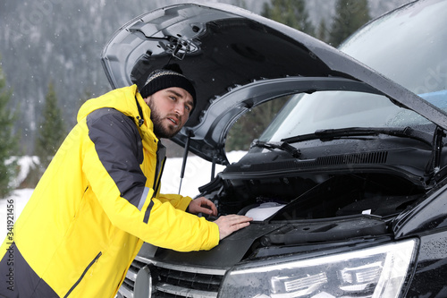 Stressed man near broken car outdoors on winter day