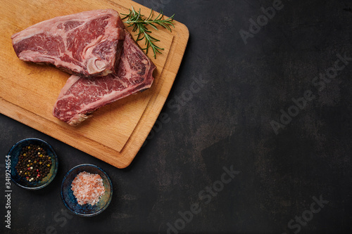 Raw Dry Aged Beef Steak. Raw Dry Aged Meat. Raw sirloin steak on a wooden board with four peppers blend, himalayan salt, and rosemary. black slate stone background