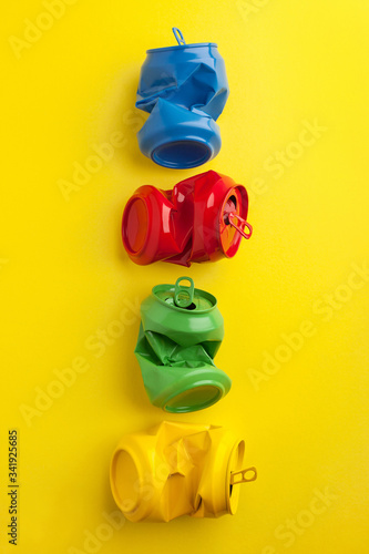 Used and crumpled different colors of red, blue, yellow and green aluminium soda can on yellow background.