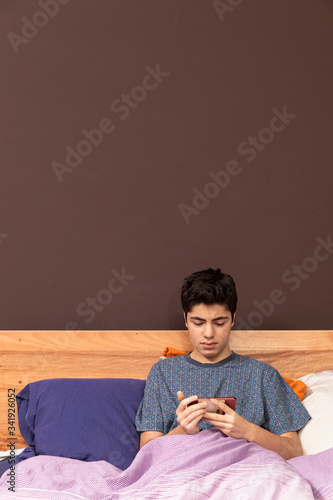 Boy at home in the bedroom. He plays with phone.