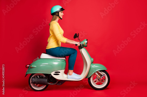 Profile side view portrait of her she nice attractive lovely confident cheerful cheery girl riding moped spending weekend isolated on bright vivid shine vibrant red color background