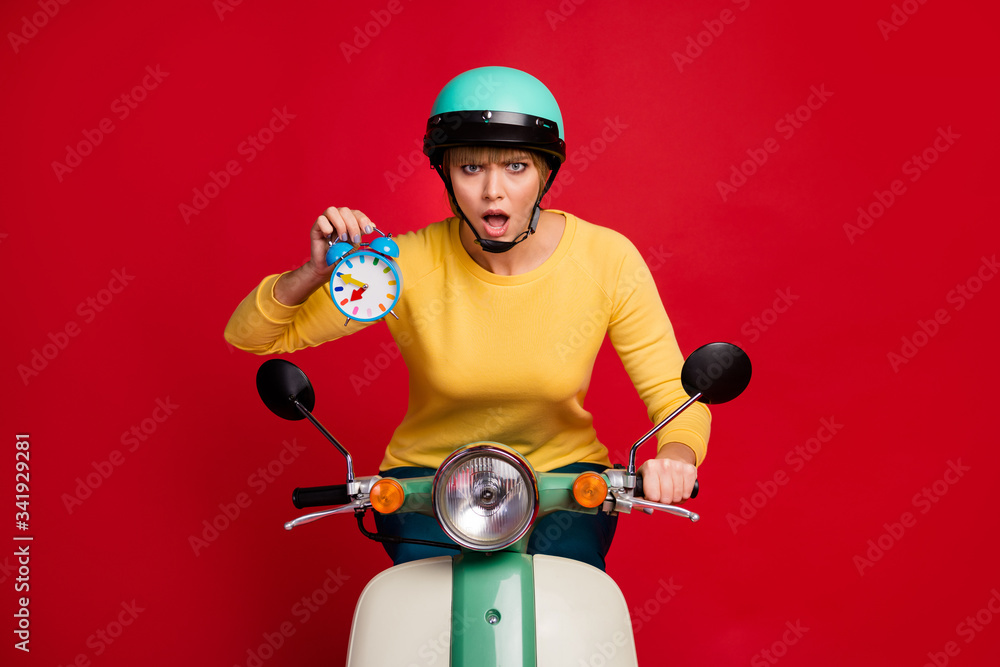 Portrait of surprised negative girl ride motorbike hold clock missed best time racing competition impressed scream omg wear yellow jumper isolated bright shine color background