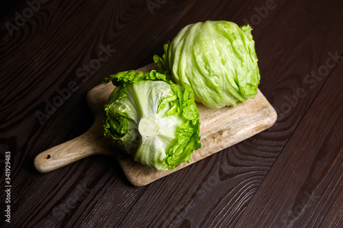 Iceberg lettuce on cutting board on wooden table background. Whole heads of fresh crisphead lettuce