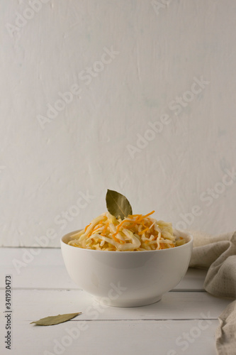 fermented white cabbage in a white bowl on a wooden white background,