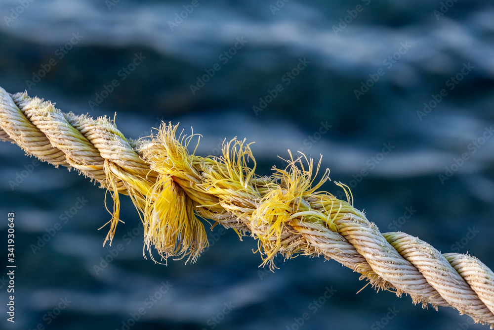 Obraz premium Frayed rope near to break on blue sea water background. Selective focus