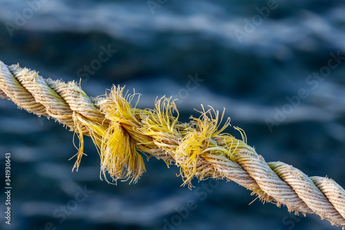 Frayed rope near to break on blue sea water background. Selective focus