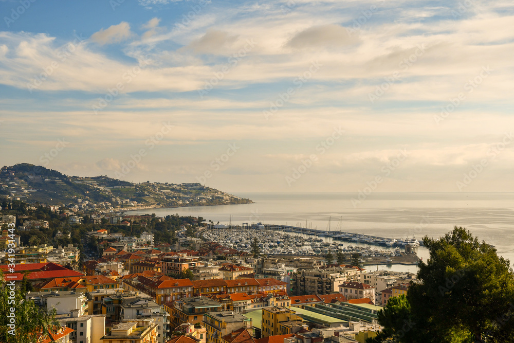 Elevated, panoramic view of the coastline of Sanremo with the tourist harbor and Capo dell'Arma cape in the background in a cloudy day, Riviera of Flowers, Imperia, Liguria, Italy