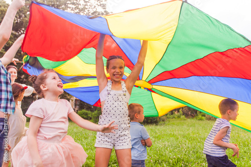 Cheerful preteen girl holding colorful canopy over kids