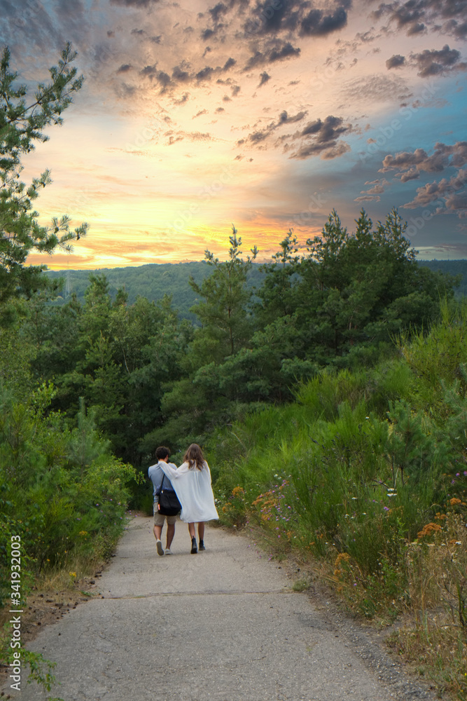 A loving couple walking down a dirt road in the forest under a dramatic sunset sky. High quality photo
