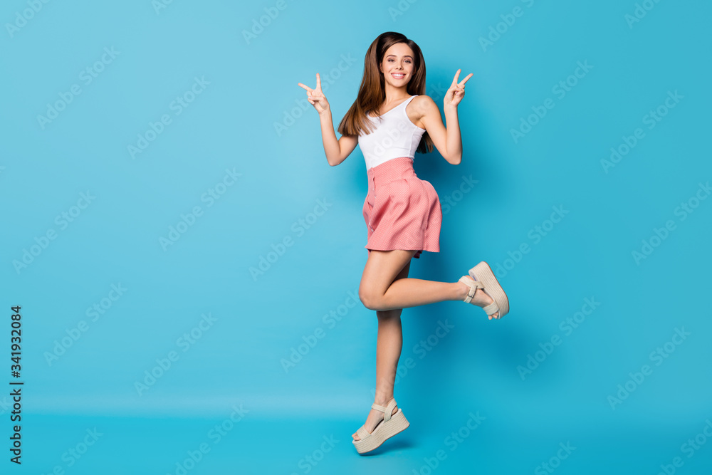 Full size photo of cheerful cute pretty girl jump make v-sign enjoy spring free time weekend holiday wear good look singlet isolated over blue color background Full size photo of cheerful cute pretty girl jump make v-sign enjoy spring free time weekend holiday wear good look singlet isolated over blue color background