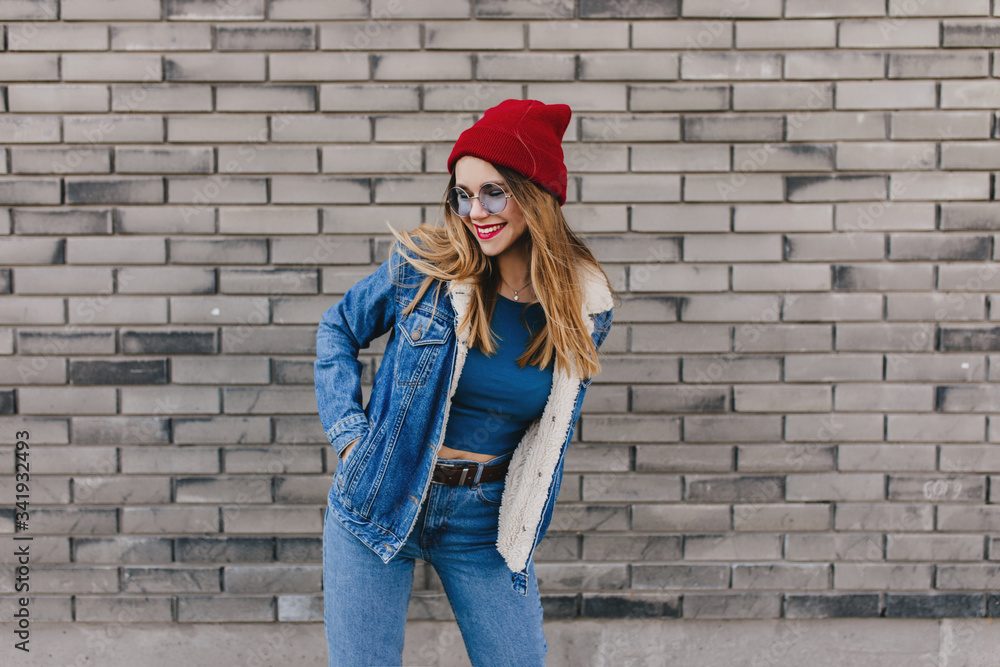 Wonderful white lady in red hat happy dancing on the street. Outdoor photo of pretty blonde girl in denim clothes having fun on brick background. Wonderful white lady in red hat happy dancing on the street. Outdoor photo of pretty blonde girl in denim clothes having fun on brick background.
