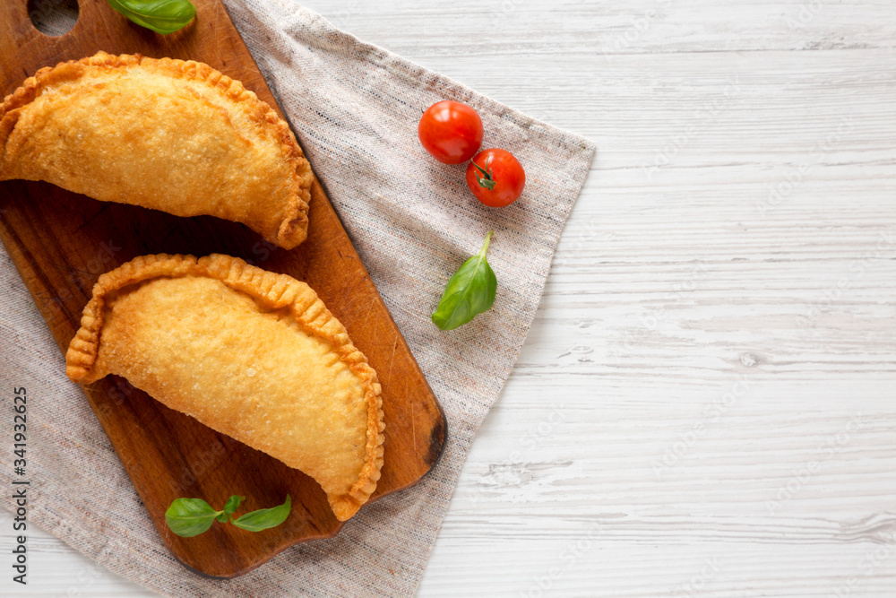 Homemade Deep Fried Italian Panzerotti Calzone on a rustic wooden board on a white wooden background, top view. Flat lay, overhead, from above. Space for text. Homemade Deep Fried Italian Panzerotti Calzone on a rustic wooden board on a white wooden background, top view. Flat lay, overhead, from above. Space for text.