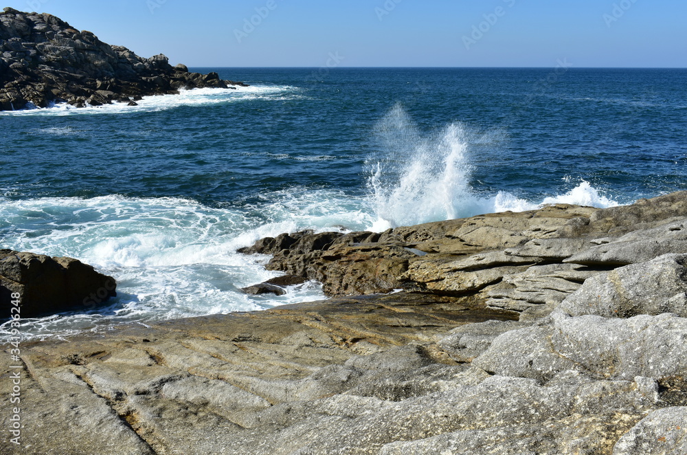Summer landscape with wild waves breaking against the rocks and blue sky. Spain.
