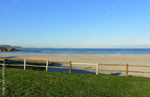 Beach with grass, wooden fence and blue sky. Arteixo, Galicia, Spain.