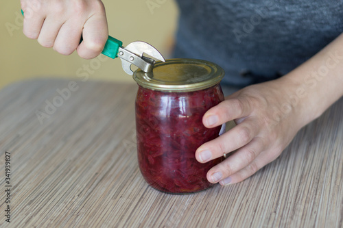 Closeup of woman opening a can in a kitchen with old style tin opener