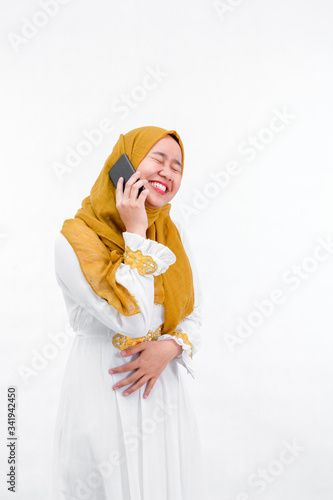 portrait of attractive asian muslim woman on white dress with hijab using a smartphone and laugh while have a call isolated over white background photo