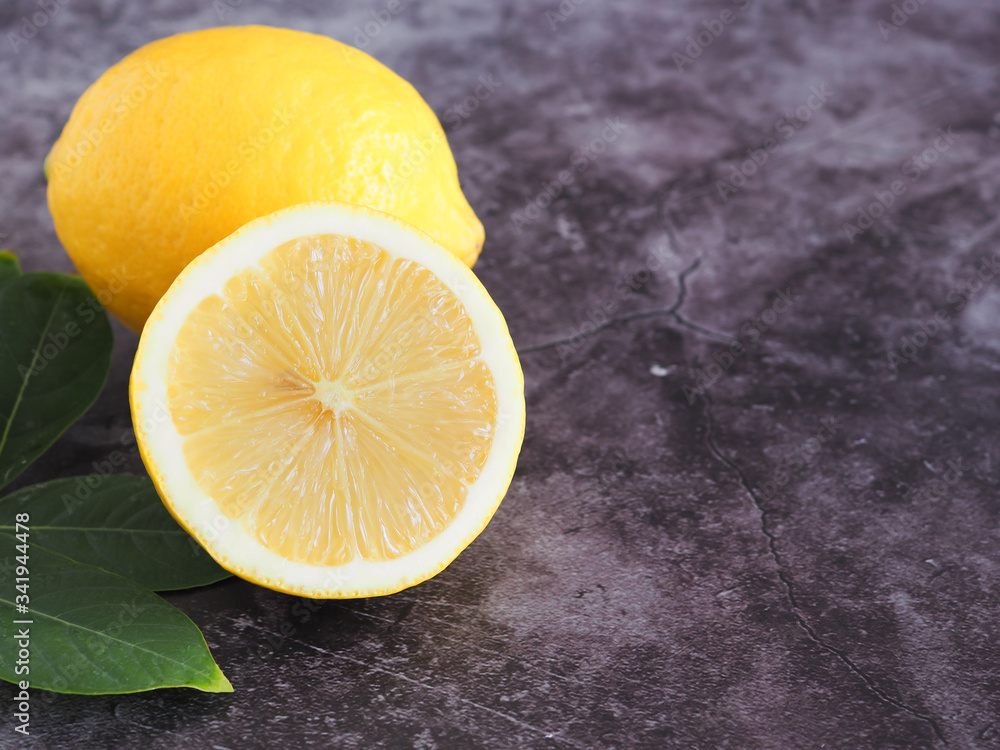Half lemon with green leaves on dark grey background with copy space. High vitamin C, which helps control weight and Reduce Cancer risk. Copy space for text.. Half lemon with green leaves on dark grey background with copy space. High vitamin C, which helps control weight and Reduce Cancer risk. Copy space for text..