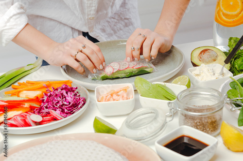 Woman's hands rolling the spring roll with fresh vegerables. Appetizing diet asian dish.