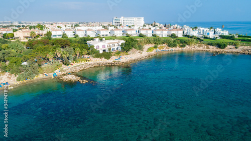 Fototapeta Naklejka Na Ścianę i Meble -  Aerial bird's eye view of Sirena beach in Protaras, Paralimni, Famagusta, Cyprus. The famous Sirina bay tourist attraction with sunbeds, golden sand, restaurant, people swimming in the sea from above.