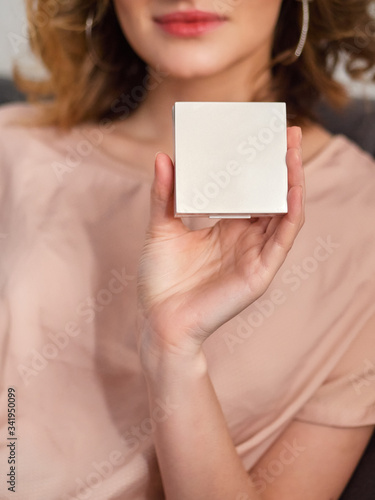 Woman's beauty blogger hand holding professional hi-end cosmetic skin tone powder box with blurred body background, warm pastel cozy tones and copyspace
