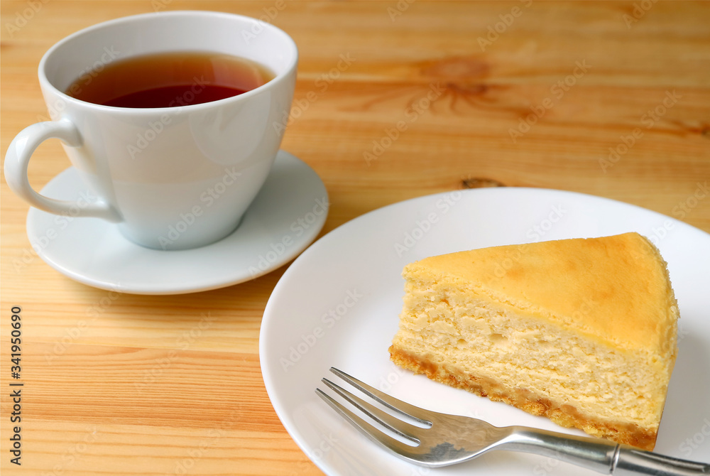Slice of baked cheesecake with a cup of hot tea served on wooden table Slice of baked cheesecake with a cup of hot tea served on wooden table