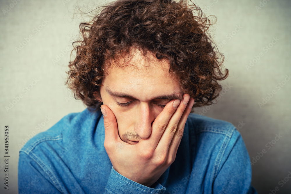 Curly young man crying, sad, covered his face with his hands. On a gray background Curly young man crying, sad, covered his face with his hands. On a gray background