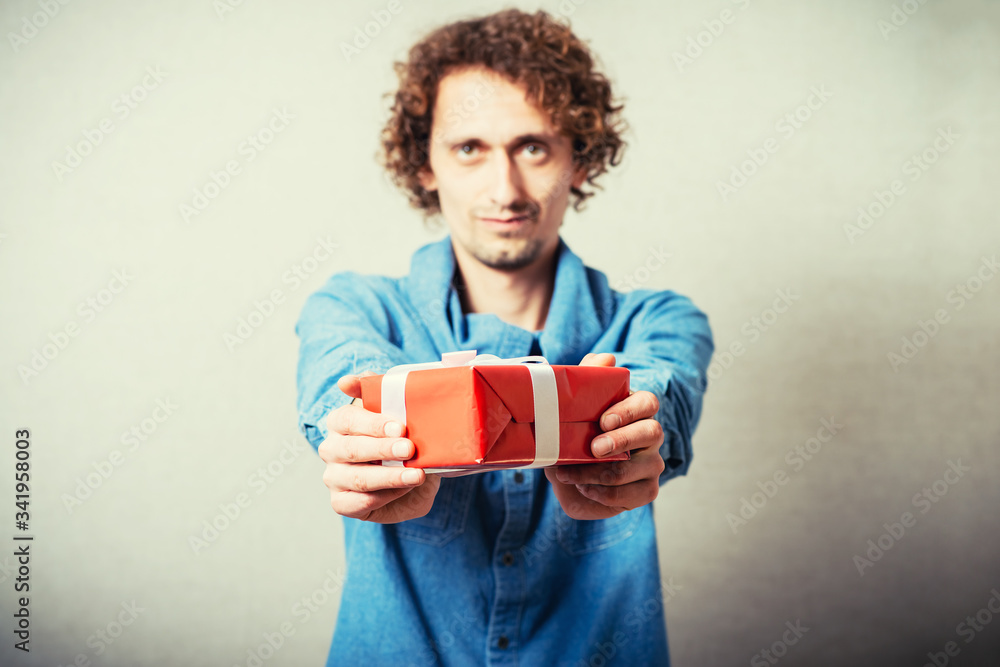 Curly man gives a gift, red box with white bow. On a gray background. Curly man gives a gift, red box with white bow. On a gray background.