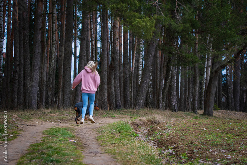 A girl in jeans runs with a Doberman in a pine forest.