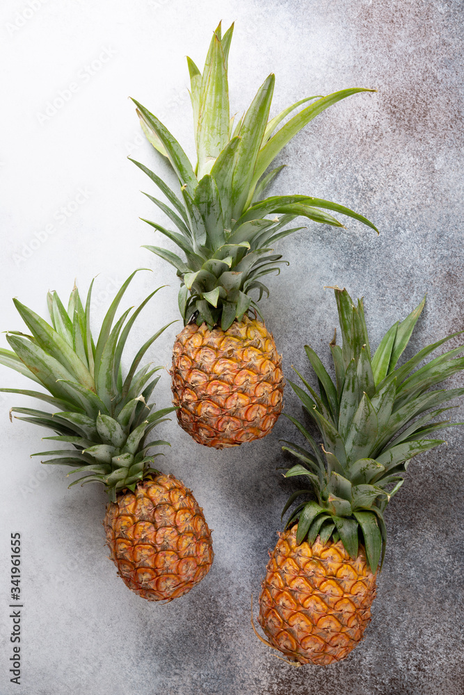 Three whole fresh ripe pineapples on concrete background. Food background. Top view, copy space. Three whole fresh ripe pineapples on concrete background. Food background. Top view, copy space.