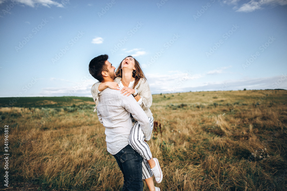 Beautiful loving couple having fun, cuddling, smiling on sky background in field. The guy and the girl hipster travel