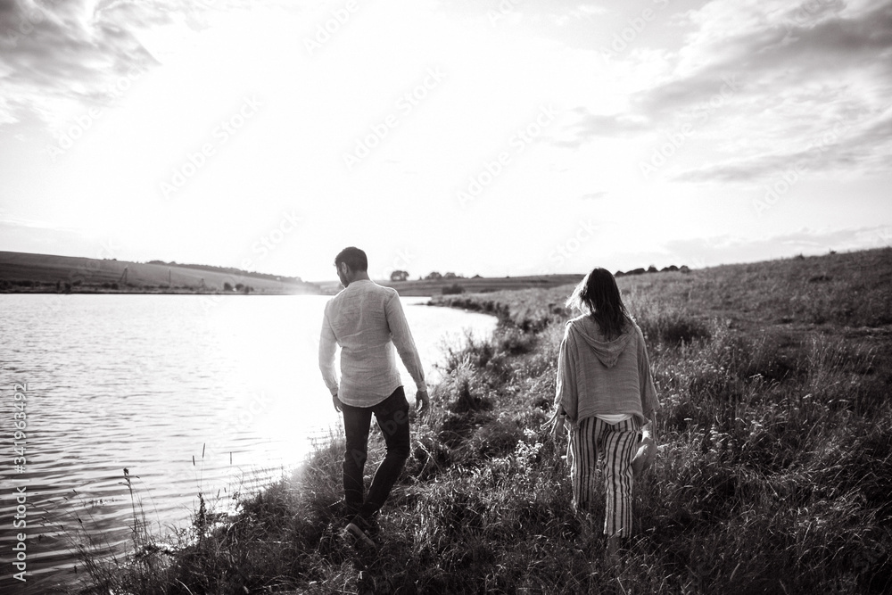 Beautiful loving couple walking on the shore, hugging, smiling on the sky background in the field. The guy and the girl hipster travel Beautiful loving couple walking on the shore, hugging, smiling on the sky background in the field. The guy and the girl hipster travel