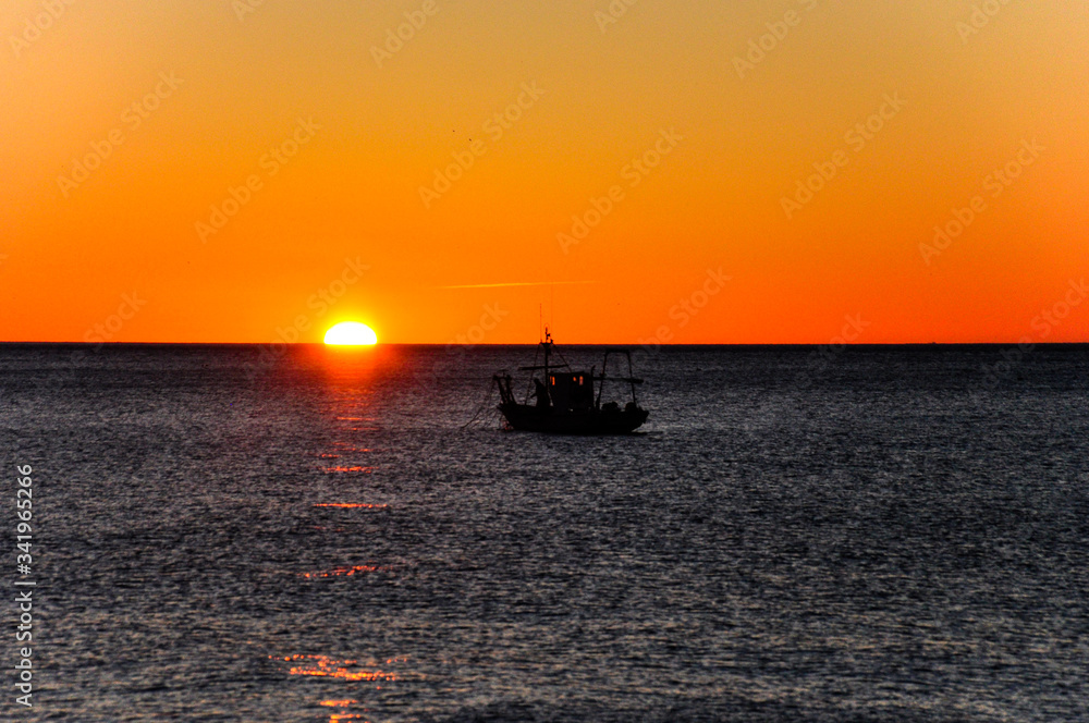 Dark silhouette of a fishing boat at sea during sunrise