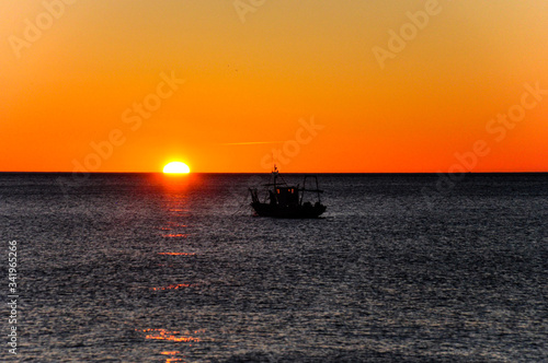 Dark silhouette of a fishing boat at sea during sunrise © Andrei