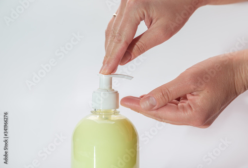 Hands push the dispenser on a yellow bottle with liquid soap. Horizontal orientation.