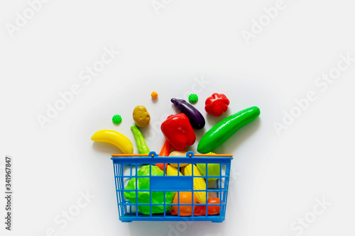 Still life with the image of colorful plastic children's fruit and vegetable toys in a basket on a white background. Top view with copy space.