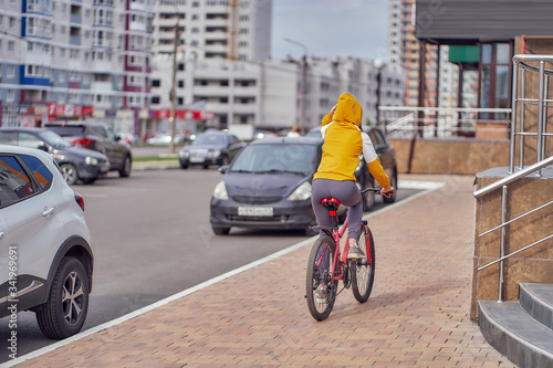 Rear view of a girl in a hood riding a bicycle in the yard.