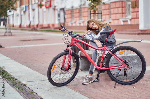 The athlete girl posing on a bench in the city with bike