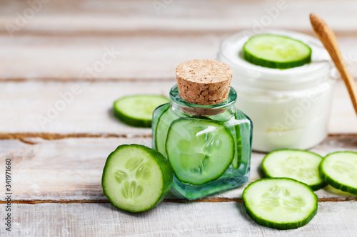 Concept of natural organic ingredients in cosmetology and home beauty treatment. Moisturizing gentle cream and mask for radiant shiny skin. Slices of fresh cucumber, wooden background, copy space