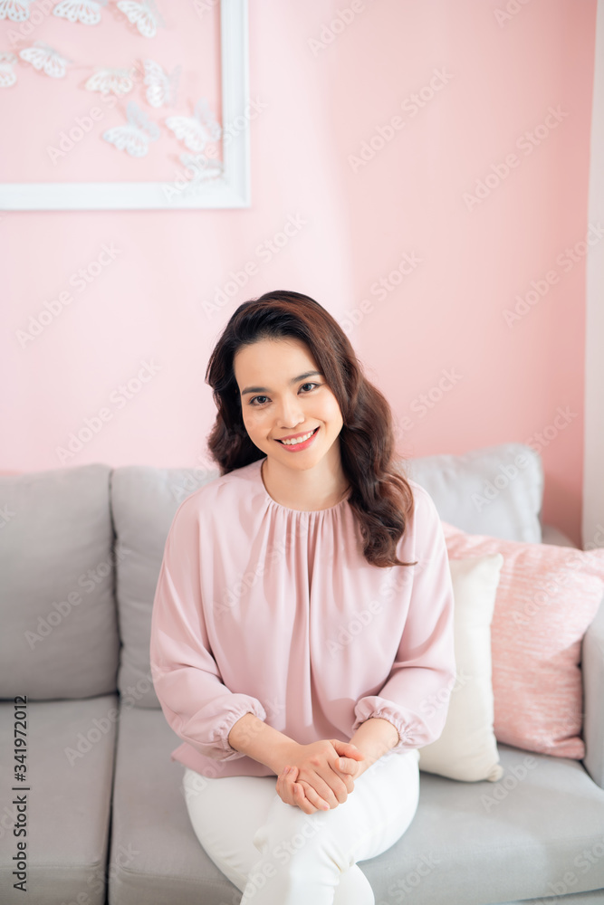Attractive young Asian woman sitting on sofa and smiling. Attractive young Asian woman sitting on sofa and smiling.