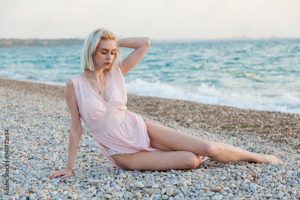 Beautiful fashionable woman in pink dress on the beach by the sea Beautiful fashionable woman in pink dress on the beach by the sea