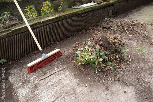 Garden broom brush with a pile of leaves in a garden yard.
