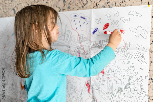 Cute little girl coloring on her wall at home.