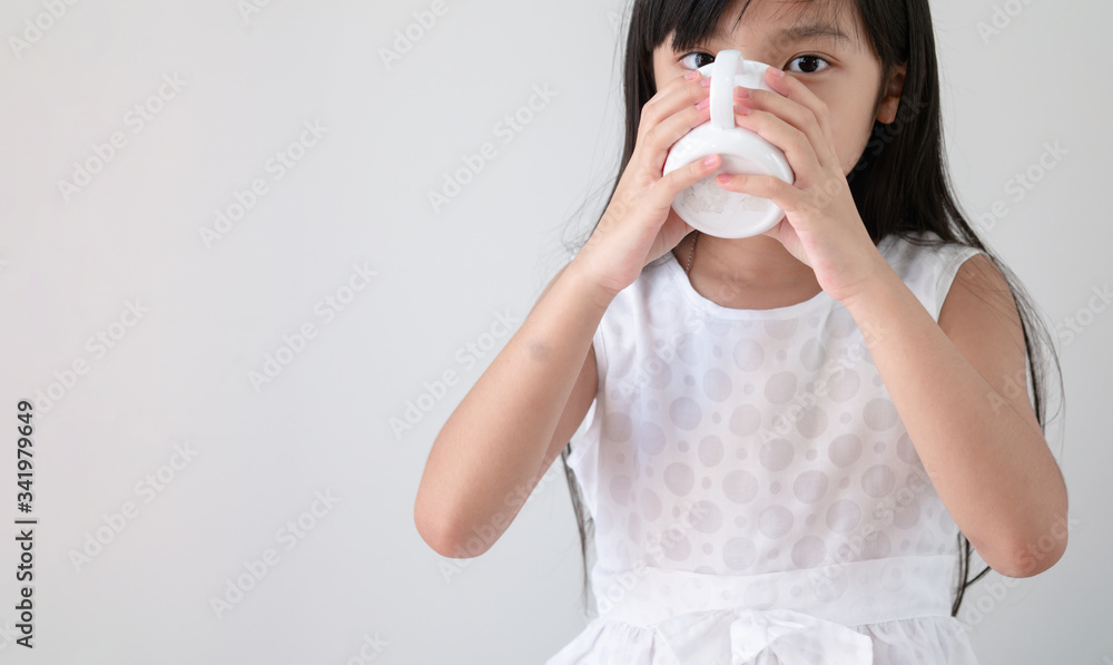 Asian girl in a white dress is drinking water or milk from a glass. Asian girl in a white dress is drinking water or milk from a glass.